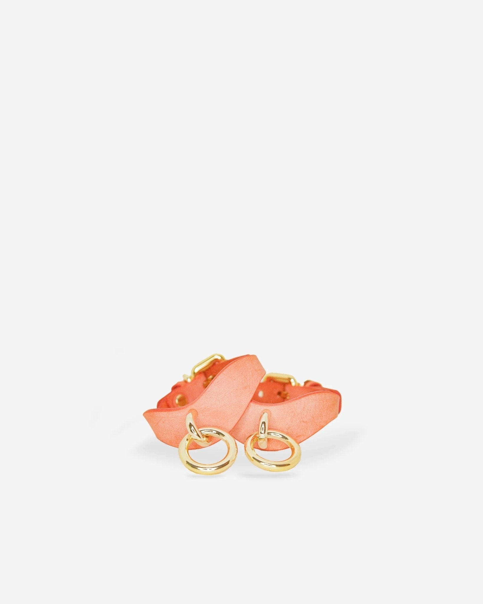 Pair of orange leather wrist cuffs with gold-tone metal rings on white background
