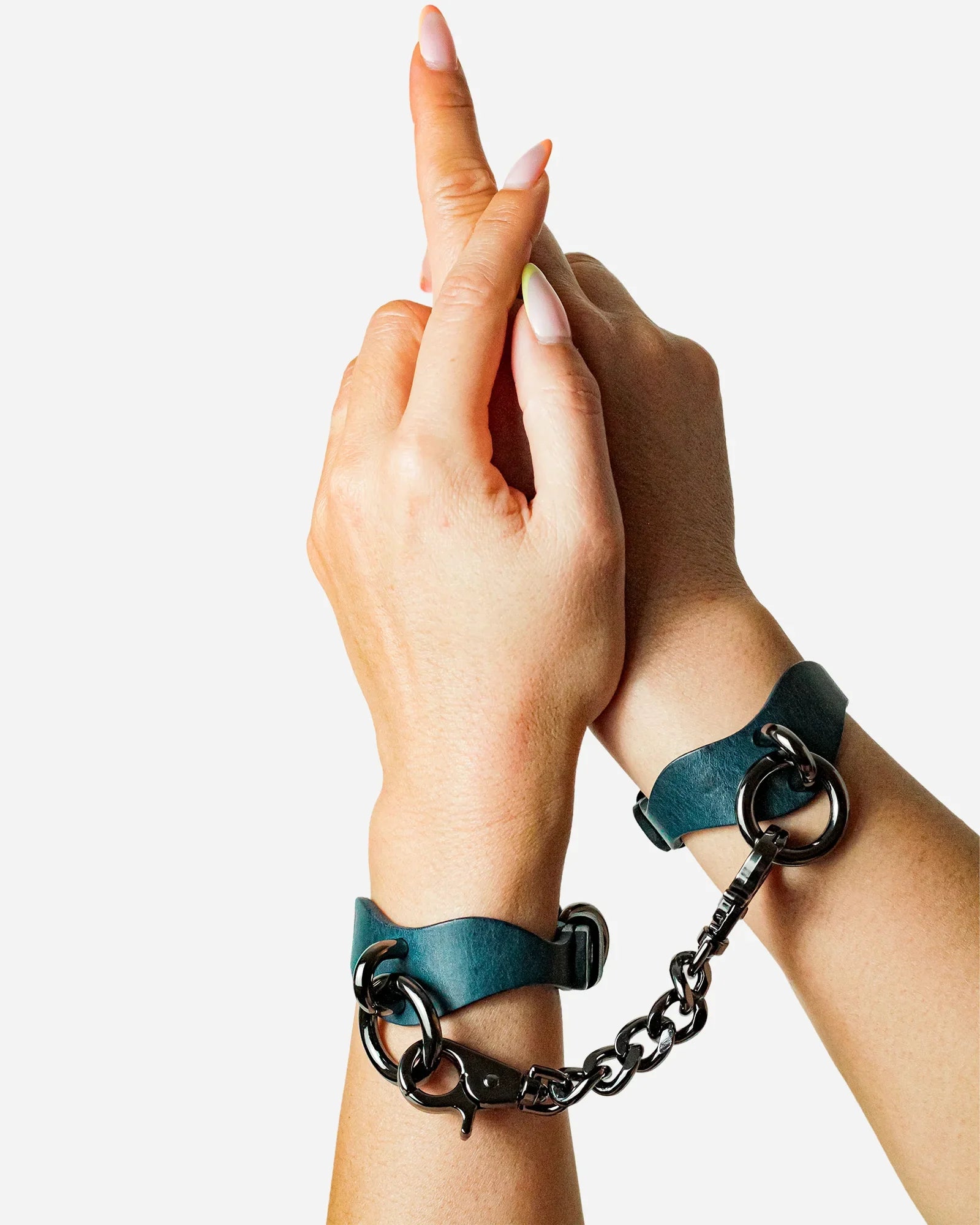 Hands wearing blue leather wrist cuffs connected by metal chain on white background