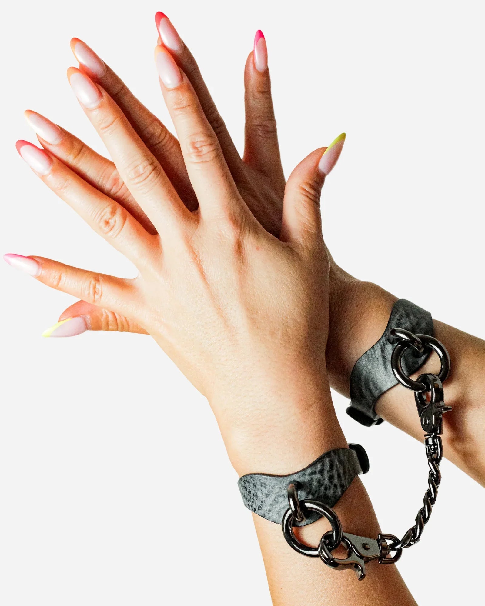 Hands wearing grey leather wrist cuffs connected by black metal chain against white background