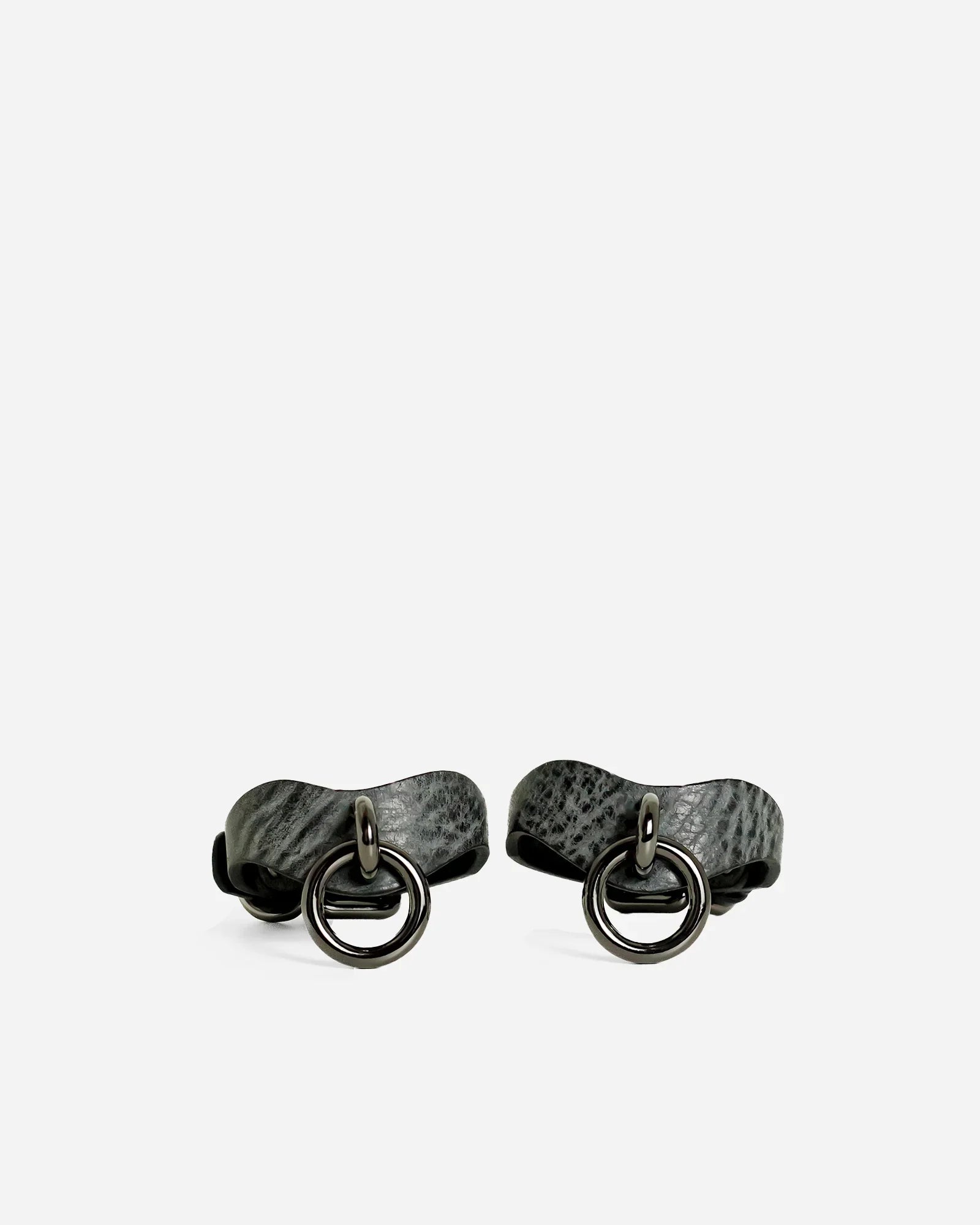 Pair of textured ash gray leather wrist cuffs with black metal O-ring hardware on white background