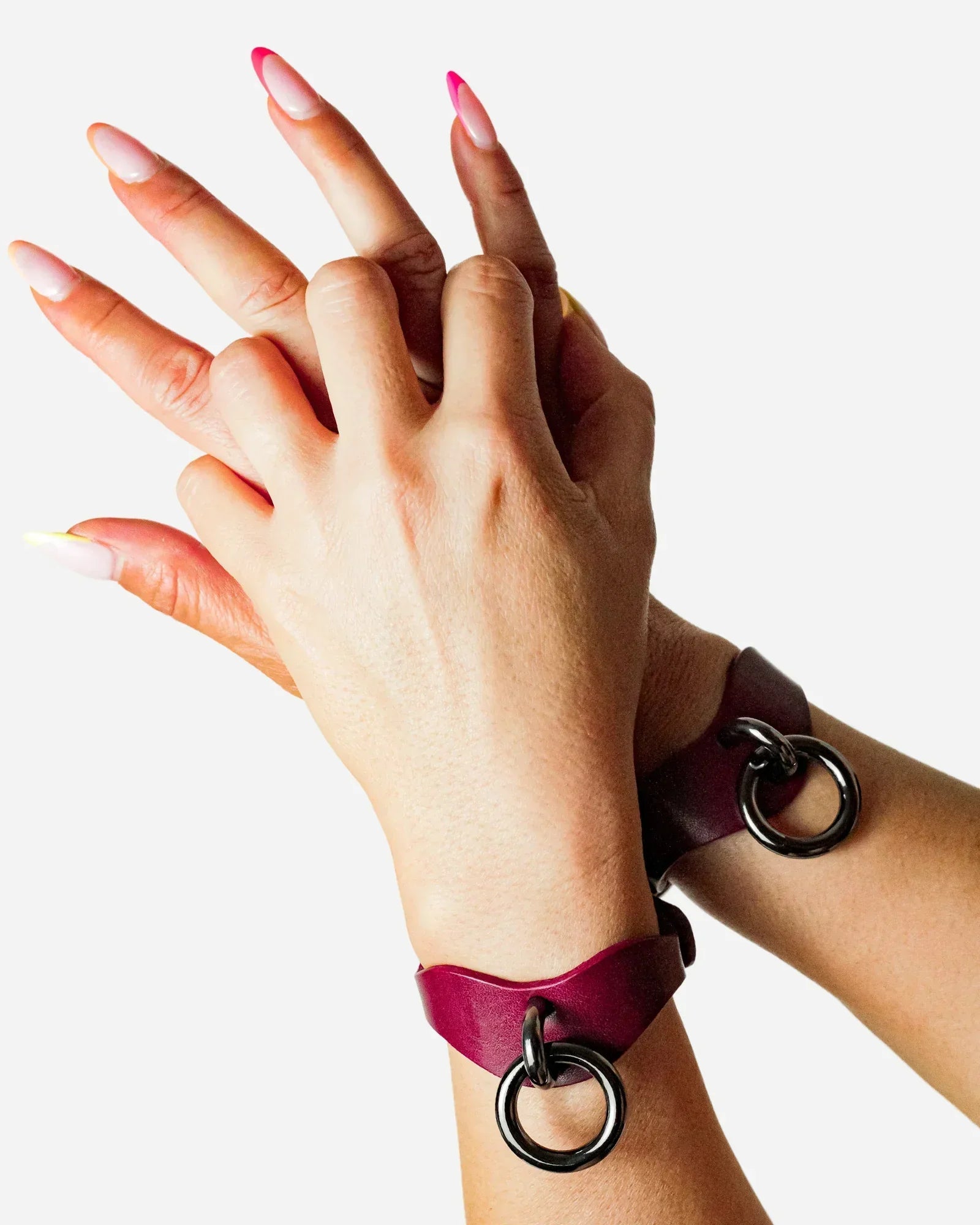 Hands wearing Bordeaux leather wrist cuffs with black metal rings against white background