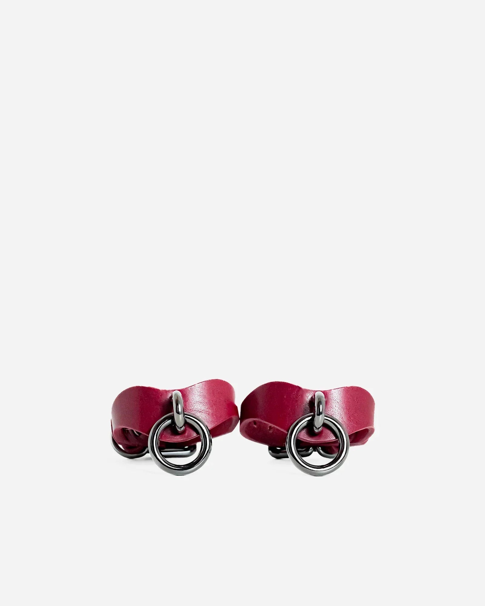 Pair of Bordeaux leather wrist cuffs with silver metal O-ring hardware on white background