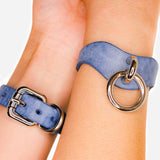 Close-up of blue leather wrist cuffs with silver metal buckle and ring on two wrists