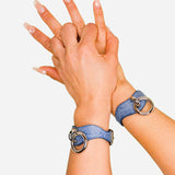 Blue leather wrist cuffs with silver rings on person's wrists against white background, showcasing leather cuffs detail