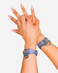 Blue leather wrist cuffs with silver rings on person's wrists against white background, showcasing leather cuffs detail