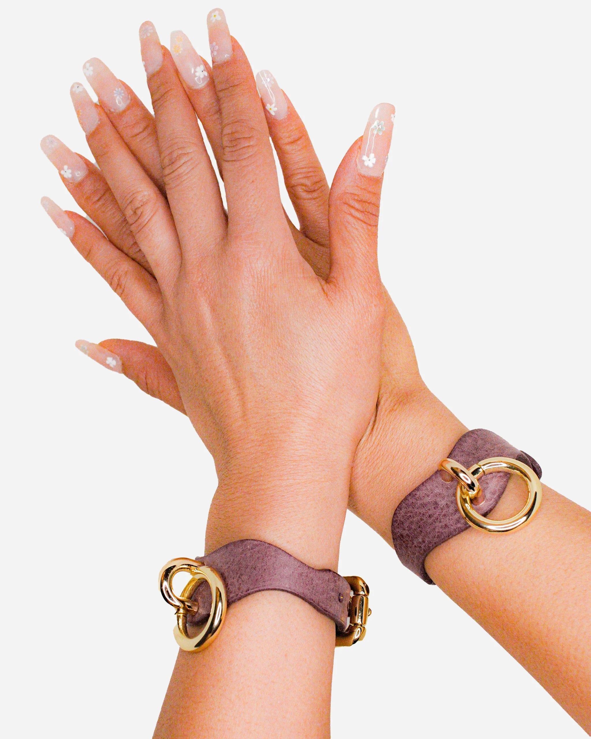 Hands wearing custom leather wrist cuffs in purple with gold rings, highlighting leather collars and cuffs