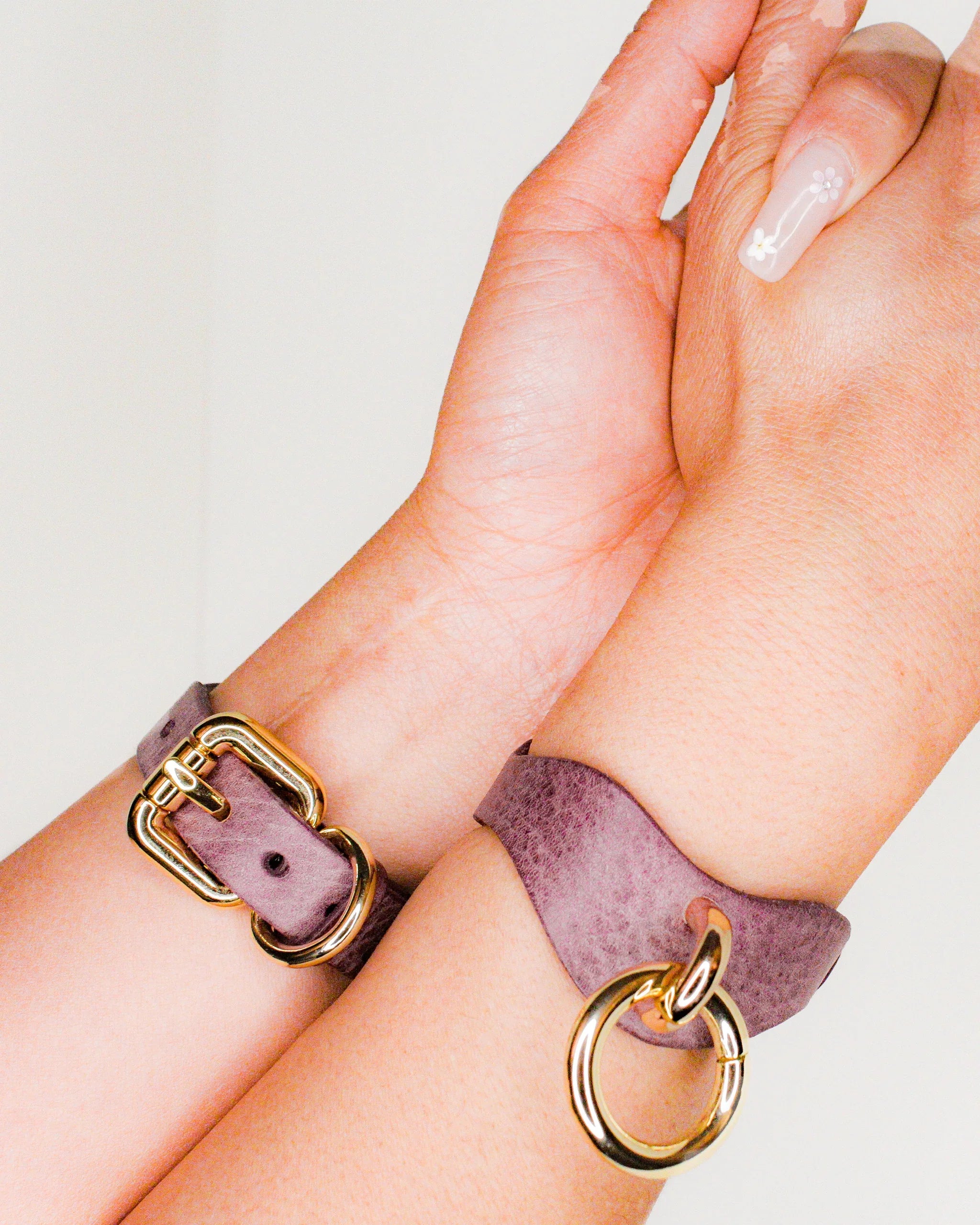 Close-up of hands wearing purple leather cuffs with gold hardware, showcasing custom leather wrist cuffs