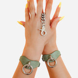 Hands wearing green leather wrist cuffs with metal rings and chain detail, styled with yellow nails
