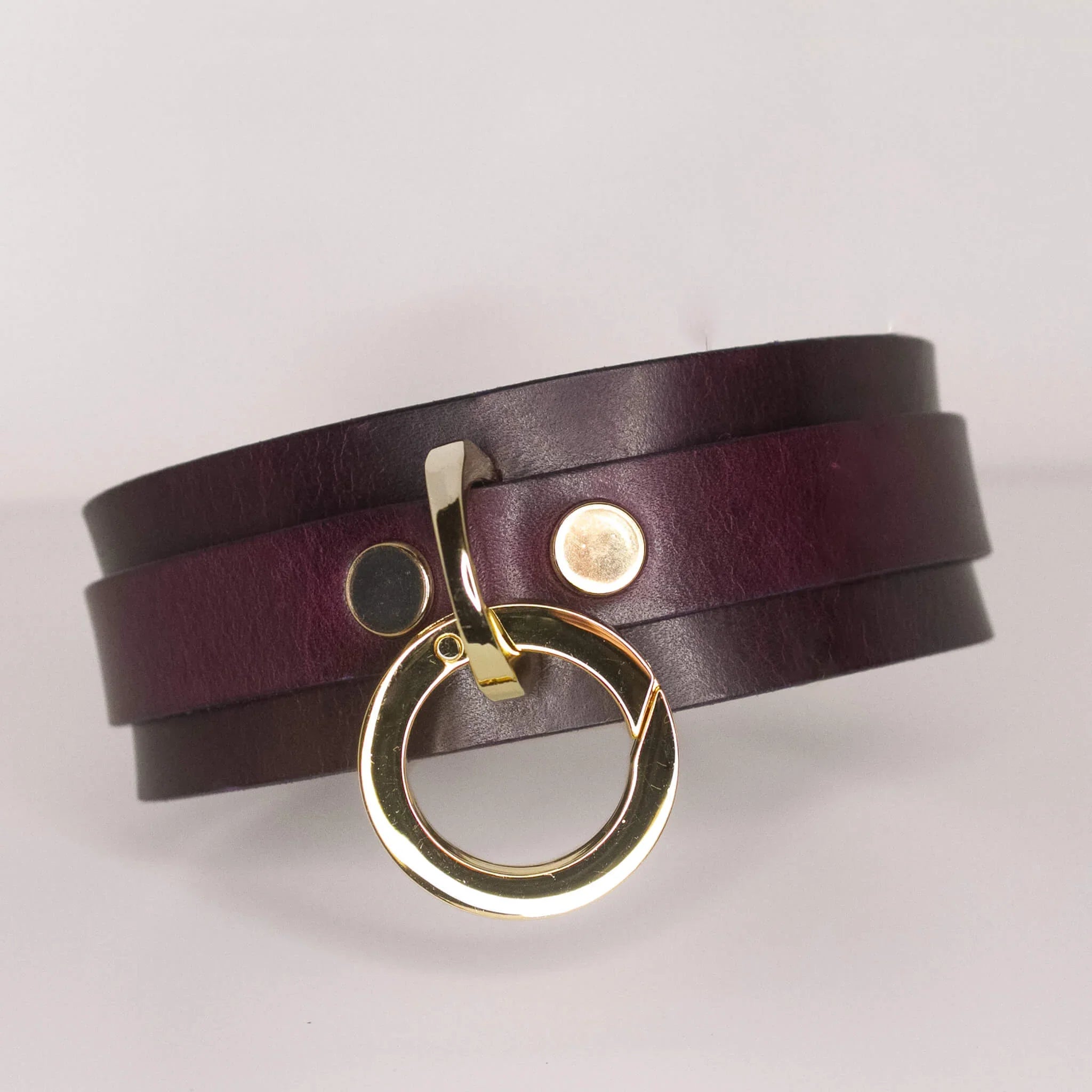 The 'Milky Way' collar showcases a rich burgundy leather with a lustrous gold-tone O-ring, set against a clean, neutral backdrop to accentuate its luxe design.