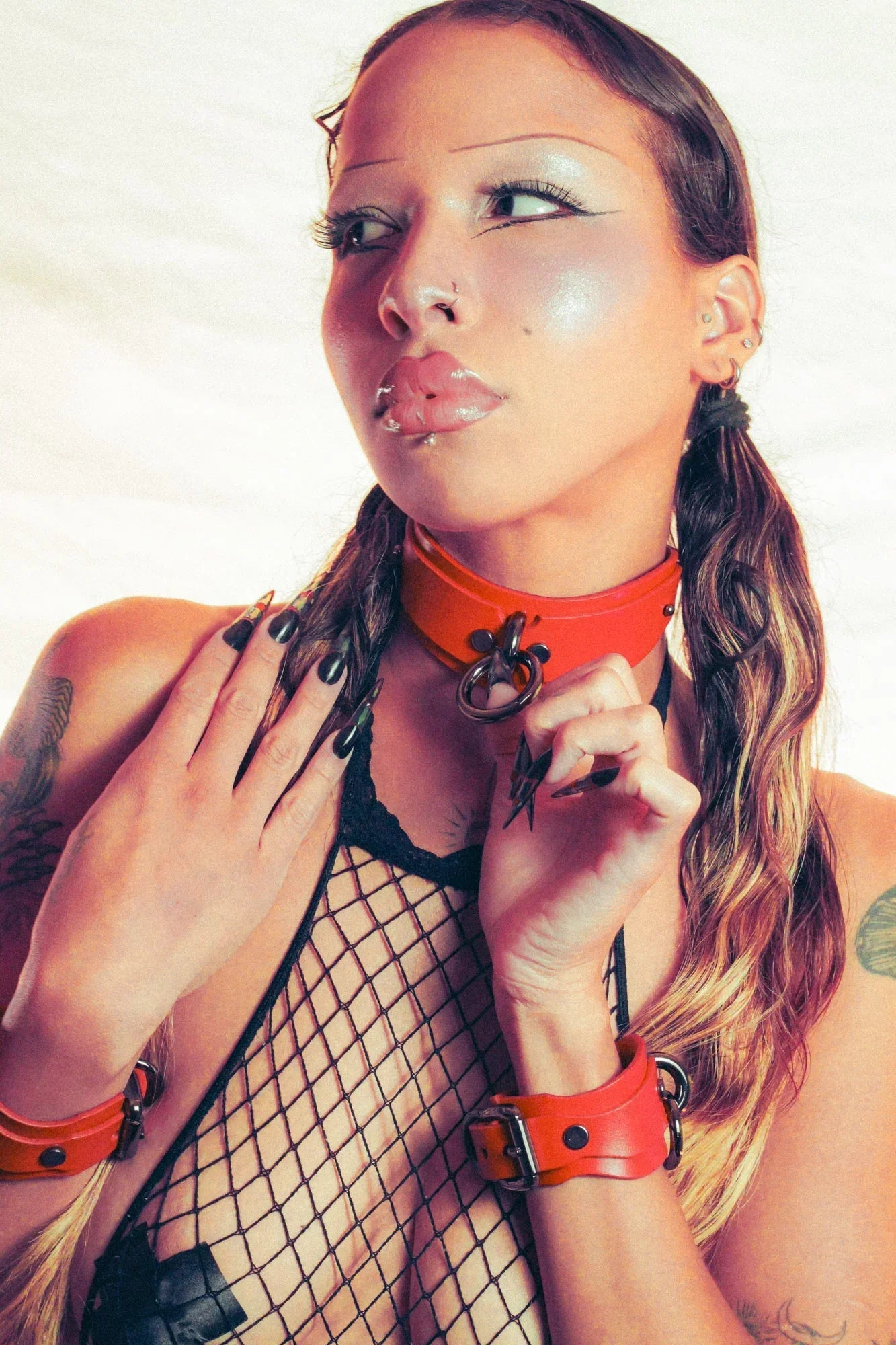 Woman wearing a red bdsm collar and black fishnet top with tattoos on a white background