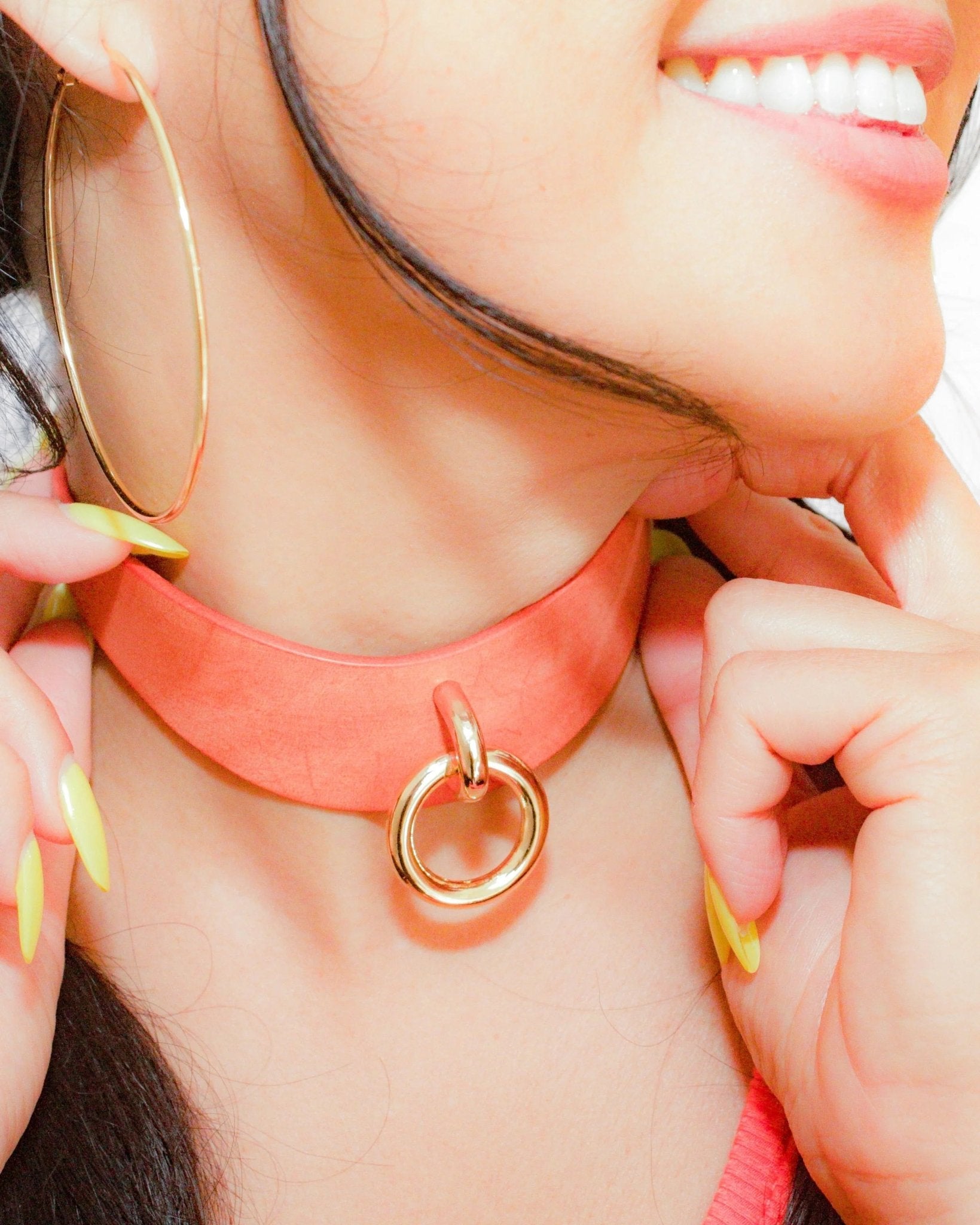 Close-up of woman wearing orange leather day collar with gold ring, showcasing custom leather collars and cuffs