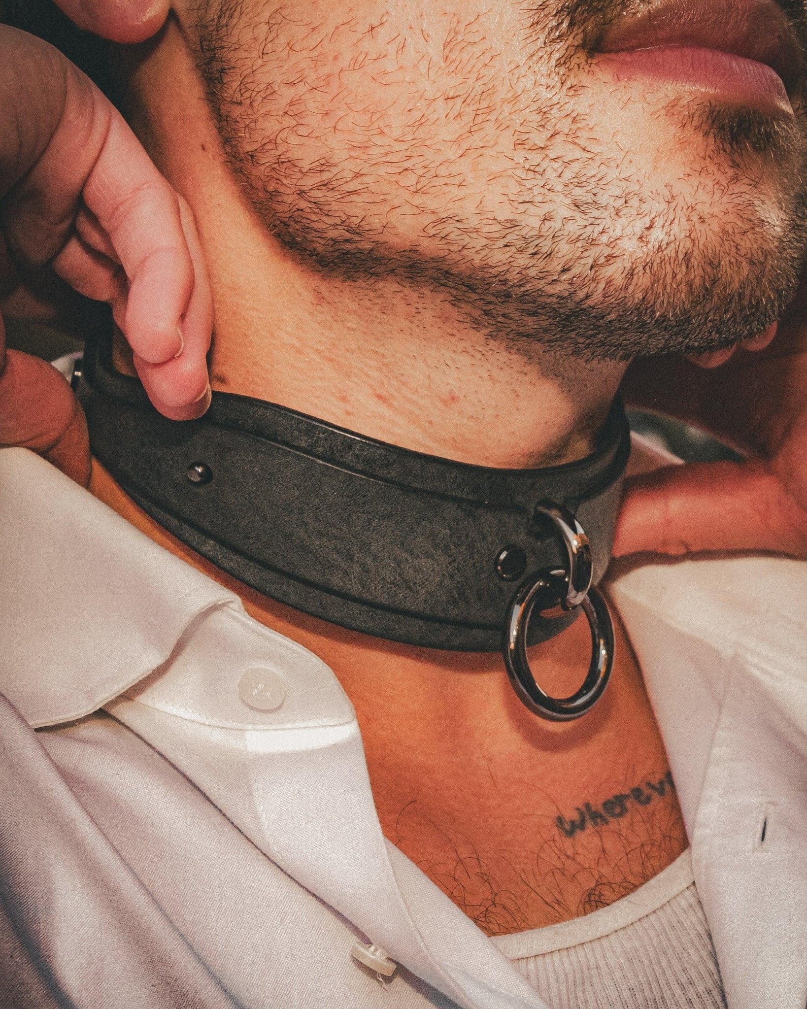 Close-up of a man wearing a black leather collar with metal ring, showcasing custom leather collars