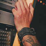 Close-up of a tattooed wrist wearing a black leather wrist cuff pressing a button on a machine