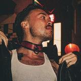 Man wearing a red leather day collar with black trim in an urban night setting, adjusting a black leather jacket