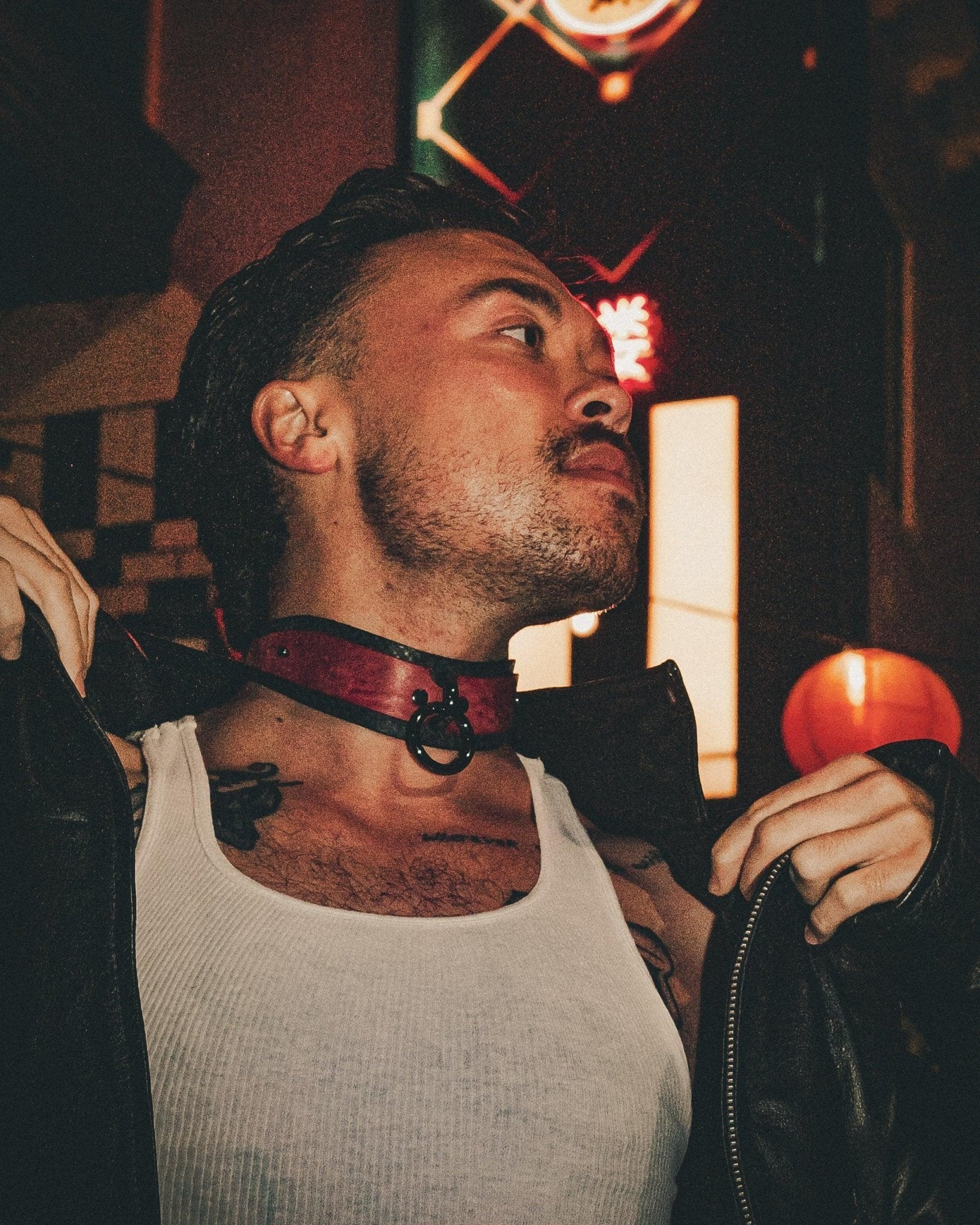 Man wearing a red leather day collar with black trim in an urban night setting, adjusting a black leather jacket
